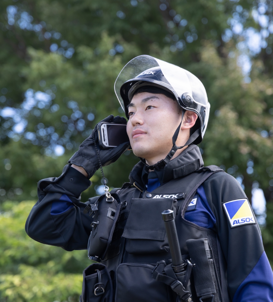 ALSOKガードマンが携帯電話で連絡を聞いている写真